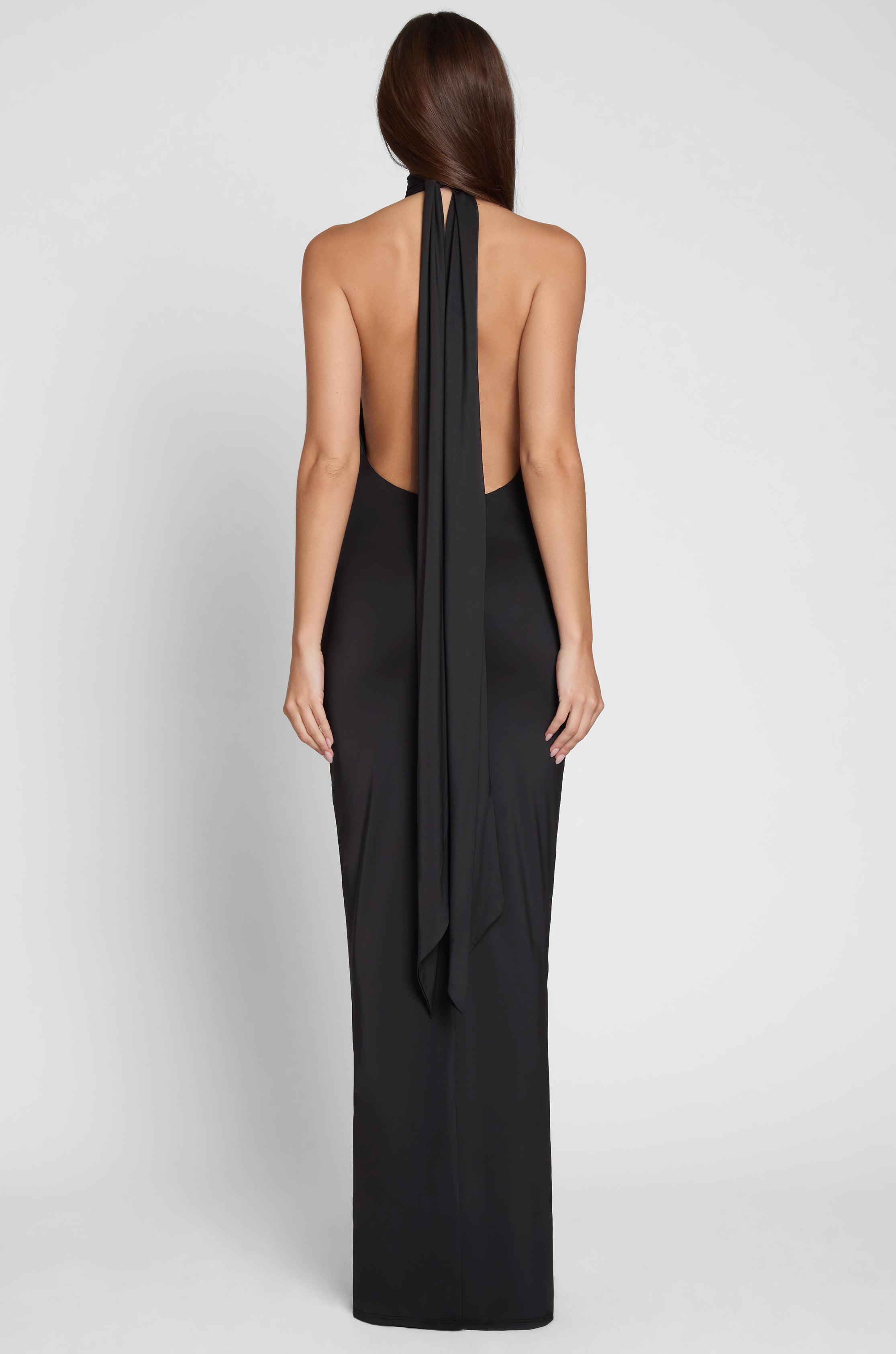 Model is wearing Alaia Drape Maxi Dress Black, back view.