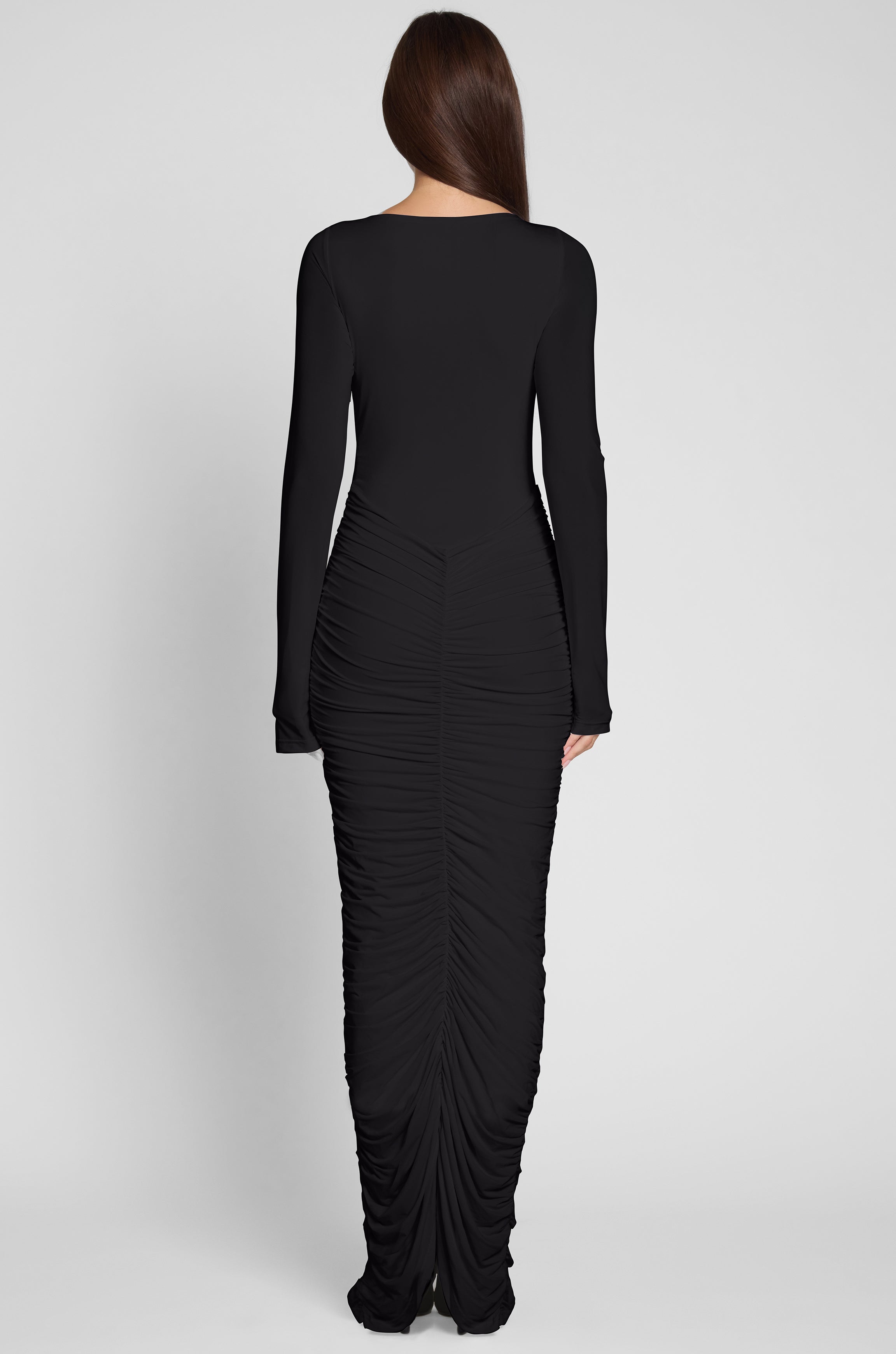 Model is wearing Rhea Ruche Maxi Dress in Black, back view.